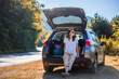 © olezzo - Happy young woman driver traveler in sunglasses standing near open car trunk. Road trips and summer holidays