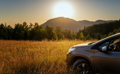 Beige gray car standing on the field at sunset with mountain view, car travel trip concept