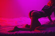 slender girl with a sexy ass in erotic underwear poses beautifully on a bed in a bedroom with neon colored light