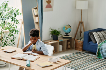 Wall Mural - African little boy sitting at desk in his room and preparing his homework reading a book