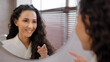 © Yuliia - Young happy confident woman standing in bathroom looking in mirror rehearsing speech instructs preparing for interview says inspiring words motivates to win winks at reflection morning routine concept