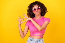 Photo Of Pretty Shiny Girl Dressed Pink T-shirt Dark Glasses Sending Kiss Showing Arms Heart Isolated Yellow Color Background