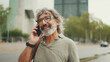 © Andrii Nekrasov - Friendly middle aged man with gray hair and beard wearing casual clothes using his mobile phone. Mature gentleman in eyeglasses talking on cell phone outdoors