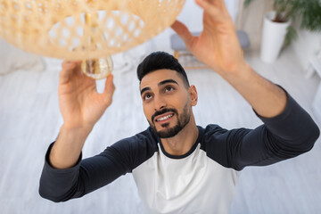 Wall Mural - High angle view of smiling arabian man changing lightbulb at home