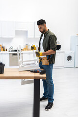 Wall Mural - Young muslim craftsman in gloves holding chair near tools at home