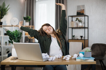 Wall Mural - Gorgeous office woman relaxing by stretching her body while sitting in front her computer laptop at the wooden working desk over comfortable living room as background.