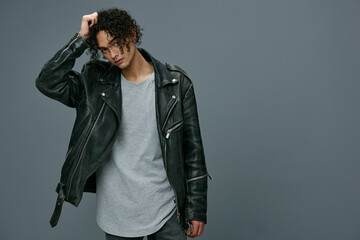 Cool fashion offer. Pretty stylish tanned curly man leather jacket looks at camera posing isolated on over gray studio background. Huge Seasonal Sale New Collection concept. Copy space for ad