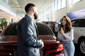 Wall Mural - a young woman persuades her husband to buy her a new car at a car dealership