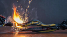 Electrical Wiring And Wires Are Lit On A Dark Background. A Short Circuit In The Twisted Wires From The Computer. Flames, Sparks And Smoke.