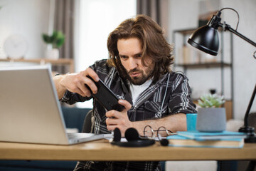 Wall Mural - Attractive bearded man playing video games on his smart phone during break in bright modern office or home. Concept of rest after hard work.