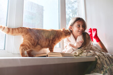 Little Girl With Red Cat Lying On Window Sill , Reading A Book Autumn Weekend With Cat At Home.