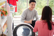 Young Asian family, Husband and wife help each other do the laundry. Husband puts the laundry in the washing machine. He looks happily at his wife who is sorting out the types of clothes.
