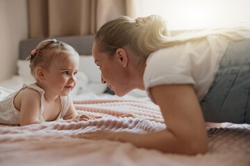 Young mother smiling and playing with her baby while lying in bed at home