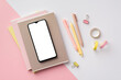 © ActionGP - Back to school concept. Top view photo of smartphone over stack of copybooks pens binder clips and adhesive tape on bicolor pink and white background with empty space