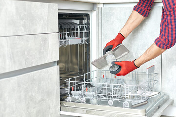 Concept maintenance service of home appliances. Worker cleans filter in the dishwasher. Male repairman checking food residue filters.