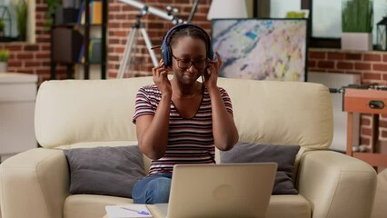 Poster - African american woman listening to music and working remotely on laptop, using internet network to do remote business job. Browsing online website and wearing headphones at home.
