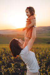 Wall Mural - Mom lifted her daughter up, holding in her arms and looking lovingly at the child. Portrait in the corn field. Happy family outdoors. Happy family, childhood