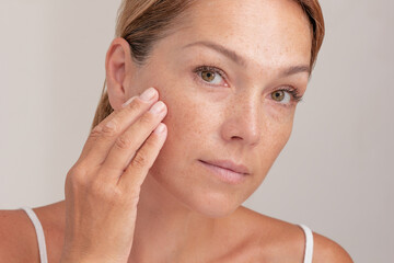 portrait of cropped caucasian middle aged woman face with freckles touching skin by hand on white ba
