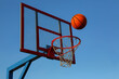 © BetterPhoto - A basketball against the blue sky is flying into the basket.
