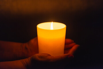 Wall Mural - Candle in female hands on black dark background.Prayers candle in hands.