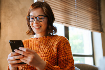 White woman smiling and using mobile phone while working in office