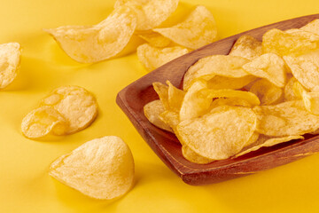 Poster - Potato chips or crisps in a bowl and scattered on a yellow background, a close-up