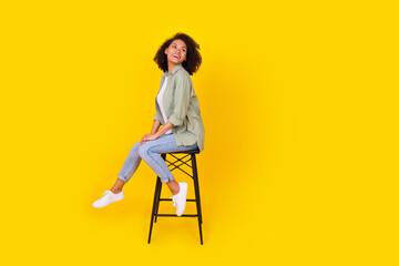 full length profile photo of brunette lady sit on chair look up wear shirt jeans boots isolated on y
