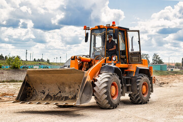 Wall Mural - A large front loader transports crushed stone or gravel in a bucket at a construction site or concrete plant. Transportation of bulk materials. Construction equipment. Bulk cargo transportation.