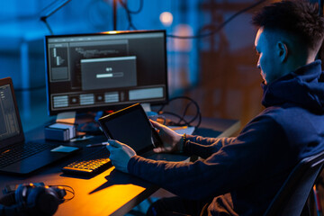 Poster - cybercrime, hacking and technology concept - close up of male hacker in dark room with tablet pc using computer virus program for cyber attack
