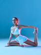 © Georgii - Beautiful tanned woman enjoying yoga or pilates. Fitness lady in white clothes on blue background.