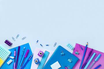 The concept of back to school. School supplies and stationery in blue and purple are arranged on a blue background in the form of a frame.