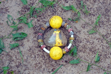 one colored plastic dirty toy rattle lies in the gray sand and green vegetation of the sandbox on the street