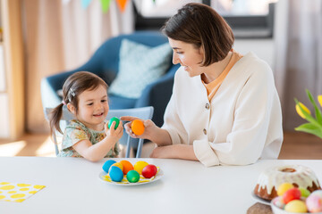 Poster - holidays, family and people concept - happy little baby daughter and mother tapping colored easter eggs at home