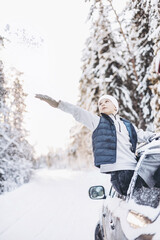 Wall Mural - Teenager boy looking out of car window traveling in winter snowy forest. Road trip adventure and local travel concept. Happy child enjoying car ride. Christmas winter holidays and New year vacation