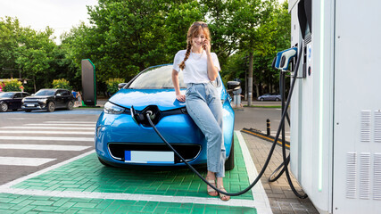 Wall Mural - Young woman with an electric car at charging station in Chisinau, Moldova