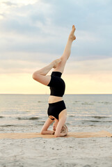 Wall Mural - fitness, sport, and healthy lifestyle concept - woman doing yoga headstand on beach over sunset