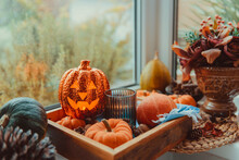 Halloween Cozy Mood Composition On The Windowsill. Lighting Jack-o-lantern, Decorative Pumpkins, Cones, Candles On Wooden Tray. Hygge Halloween Home Decor. Selective Focus.