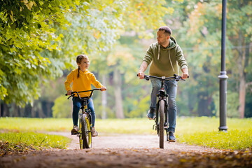 Happy father and daughter ride bicycles in autumn park on sunny day.