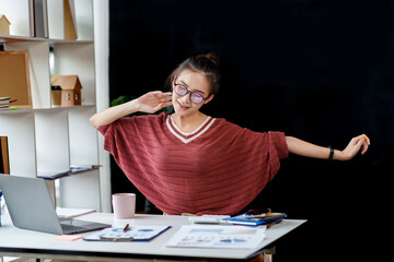 Wall Mural - Asian business woman stretches her arms to relax her tired muscles from working at a desk all day at the office.