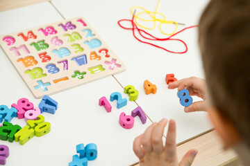 Wall Mural - kid learning numbers through game. Sensory activity with wooden numbers and shoe laces. Educations at home, pre-school education, Montessori methodology. sequence of numbers, arithmetic problems.