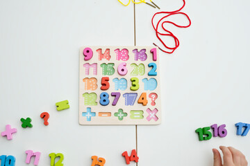 Wall Mural - kid learning numbers through game. Sensory activity with wooden numbers and shoe laces. Educations at home, pre-school education, Montessori methodology. sequence of numbers, arithmetic problems.