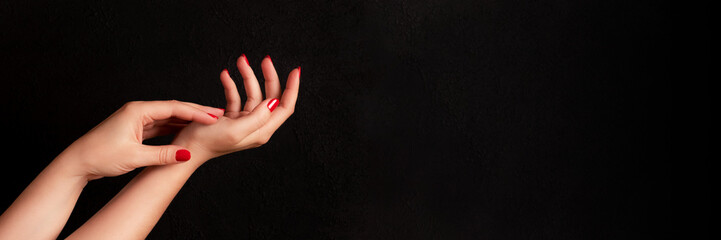 female hands with beautiful manicure - red nails on dark black background with copy space banner. wi