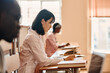 © AnnaStills - Asian medical student in white coat writing test at desk during lecture at university