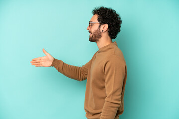 young bearded man smiling, greeting you and offering a hand shake to close a successful deal, cooperation concept