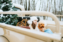 Cute Beautiful Little Armenian Girl In Winter Coat And Knitted Hat And Pet Poodle Dog Sit Near Beige Retro Pickup Truck Decorated For Christmas And New Year Vintage Interior Suitcases, Skis, Sledge
