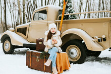 Cute Beautiful Little Armenian Girl In Winter Coat And Knitted Hat Sit Near Beige Retro Pickup Truck Decorated Christmas And New Year Vintage Interior Items, Suitcases, Skis, Sledge, Ornaments, Travel