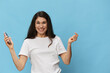 © Tatiana - portrait of a beautiful, pleasant woman with long hair, in a light T-shirt, holding a fashionable smartphone in her hands and joyfully raising her hands up. Horizontal photo on a light blue background