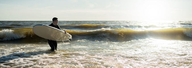 Wall Mural - A male surfer on a surfboard wetsuit goes to play sports in the sea