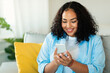 © Prostock-studio - Cheerful African American Woman Using Smartphone Sitting At Home