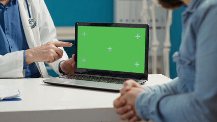 Wall Mural - Health physician and sick patient looking at greenscreen on laptop computer in medical cabinet. Blank copyspace template with isolated chroma key and mockup background. Close up.